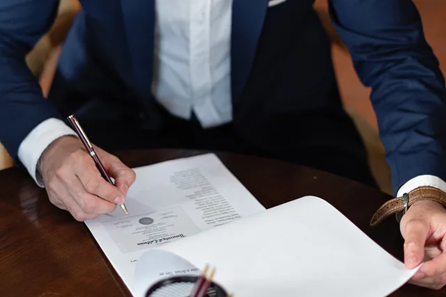 A professional individual signs legal documents at a desk in an office setting. Media buying agencies ninety day plan: from truth to handover