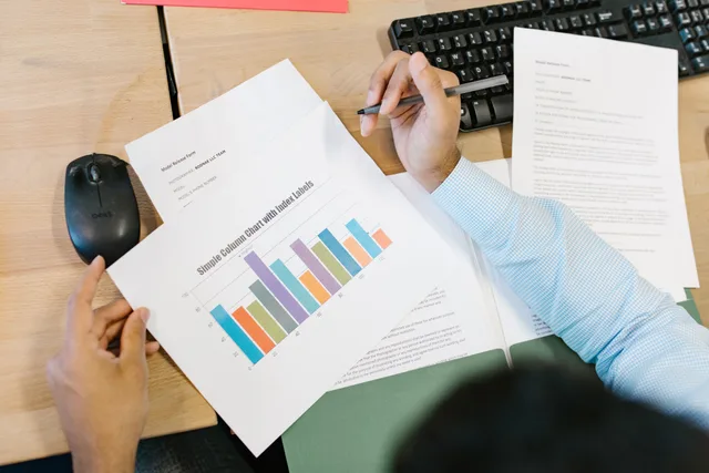 A business analyst reviews a colorful bar chart and documents at a desk, indicating data analysis. How to review media buying agencies for brief fit, not reputation